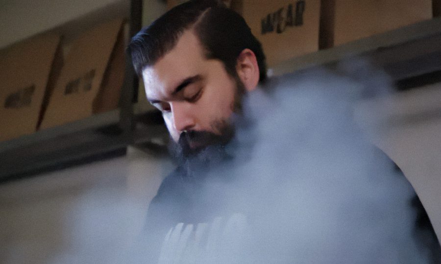 A bearded man works surrounded by steam